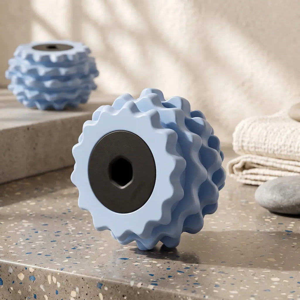 A light blue textured roller with a black center hole stands on a speckled stone surface.